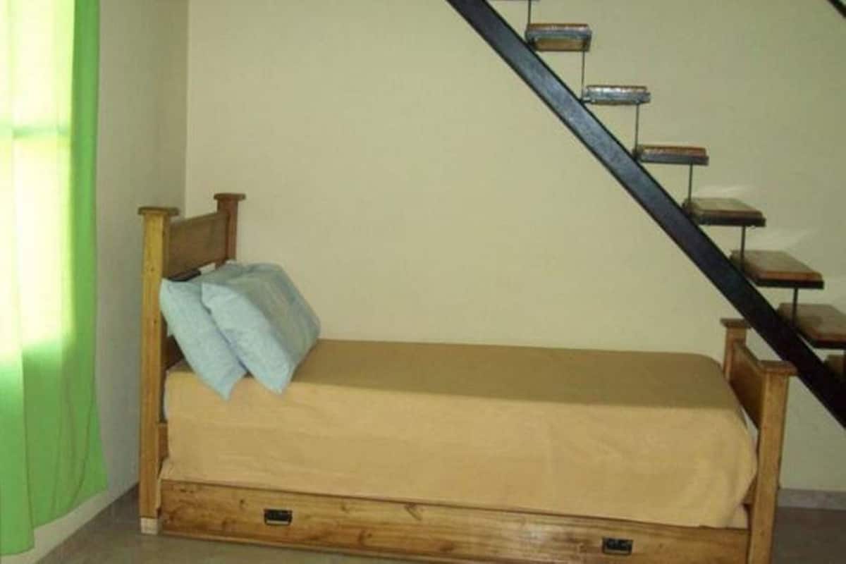 A single bed with a wooden frame and a beige mattress in a room with a staircase.