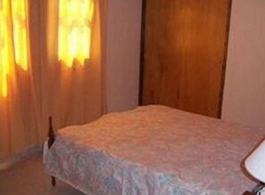Une pièce avec un lit, une armoire en bois et une fenêtre avec des rideaux.