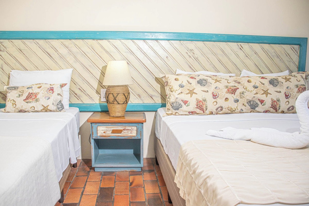 A hotel room with two beds, a nightstand, and a lamp.