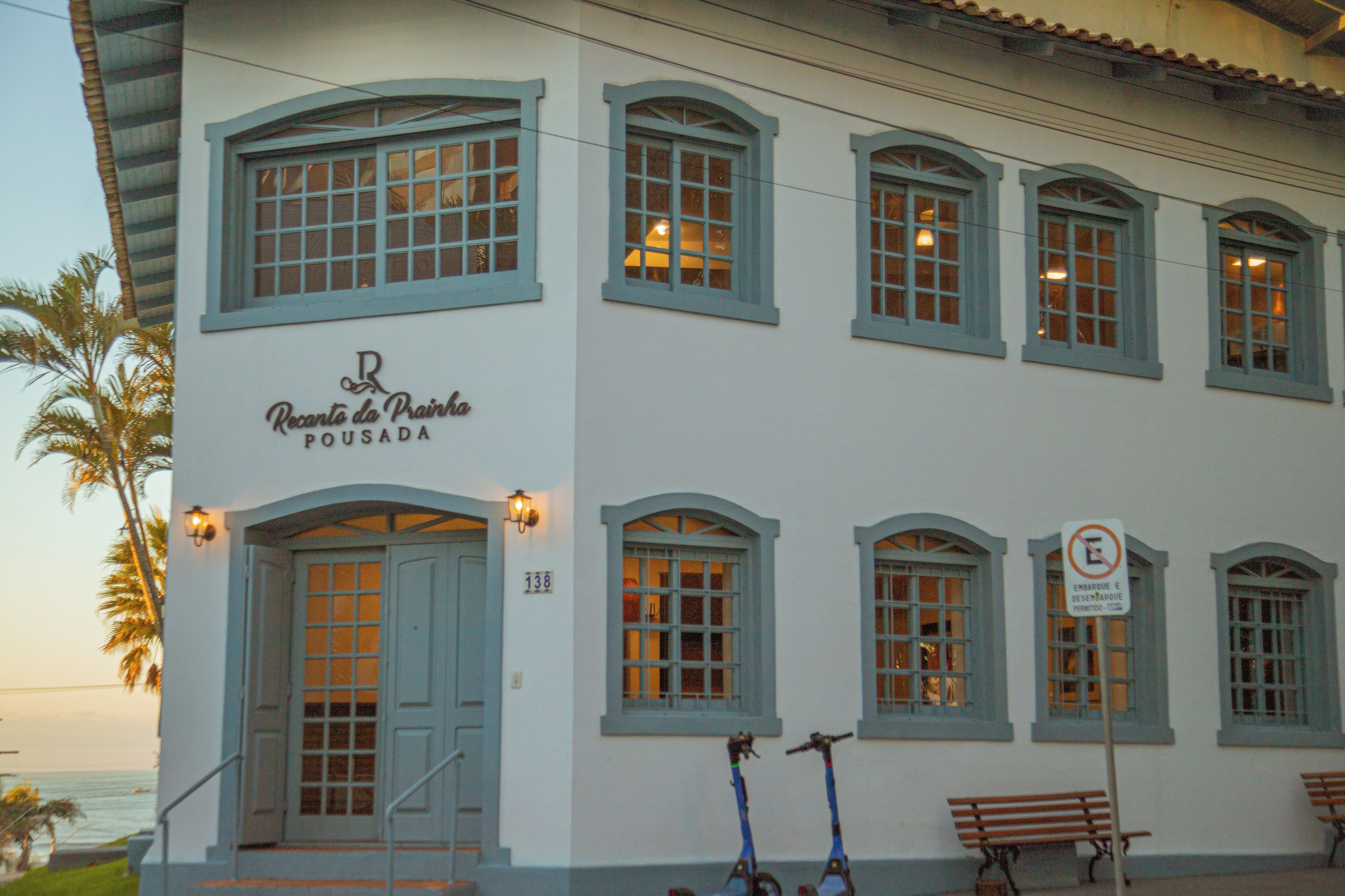 A building with multiple windows, a sign reading 'Recanto da Praia Pousada', and a no parking sign.