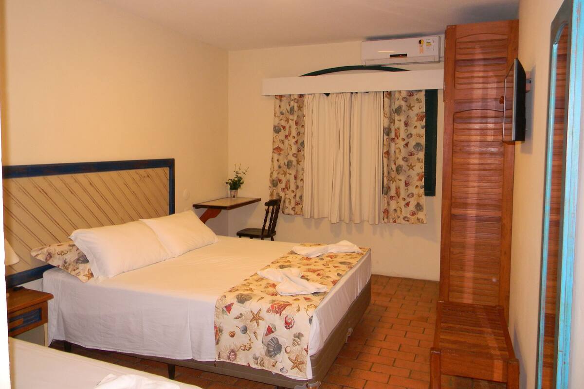 A bedroom with a bed, a desk, a chair, an air conditioning unit, and a wooden door.