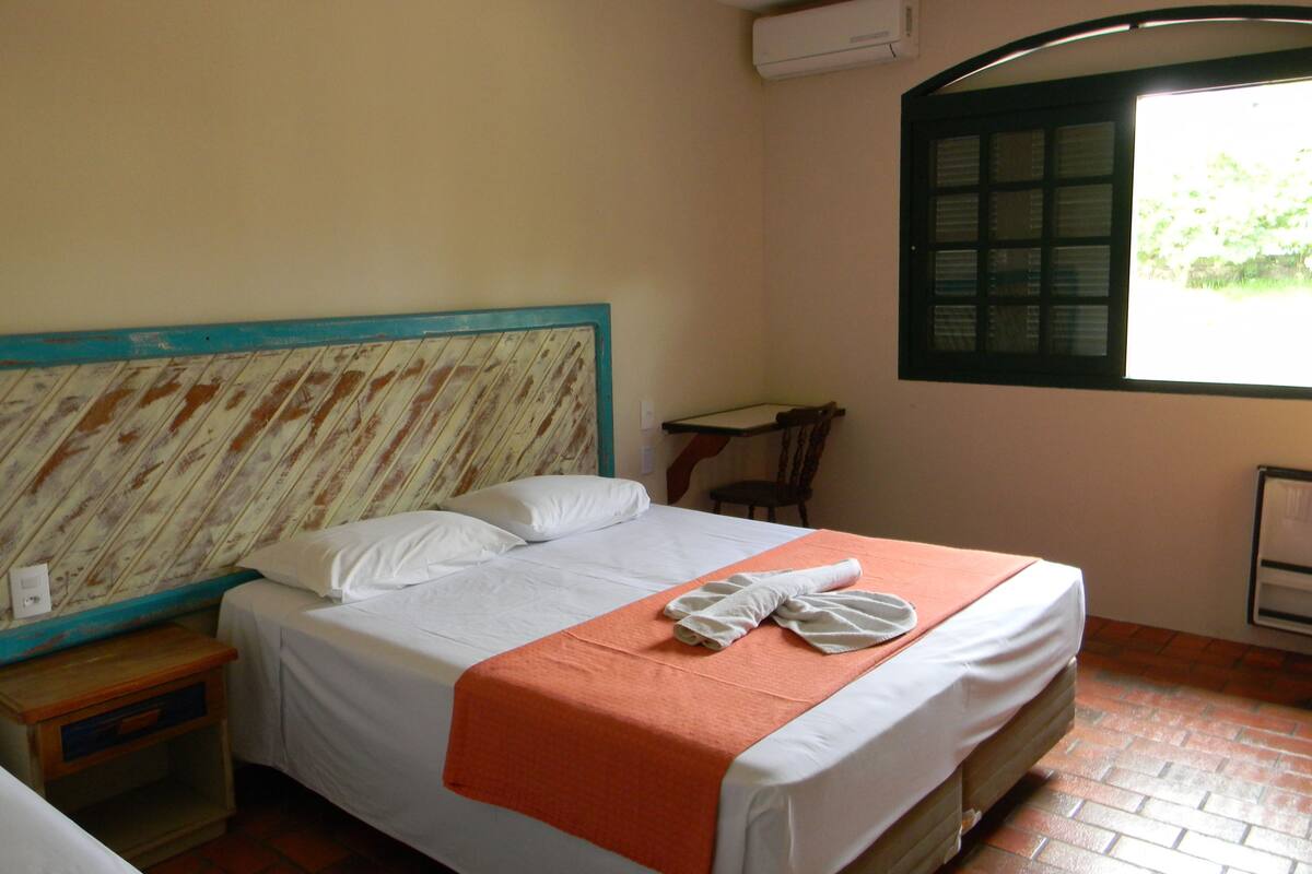 A single bed with a wooden headboard, a small table, a chair, and a window with blinds.