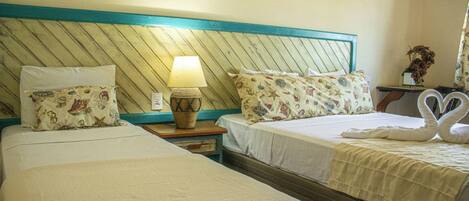 A hotel room with two beds, a nightstand with a lamp, and a decorative swan towel arrangement.