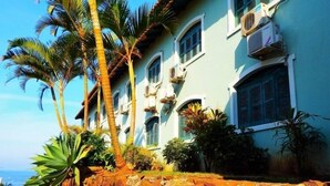 A multi-story building with air conditioning units, palm trees, and a rocky ledge. - Recanto da Prainha (Torres)