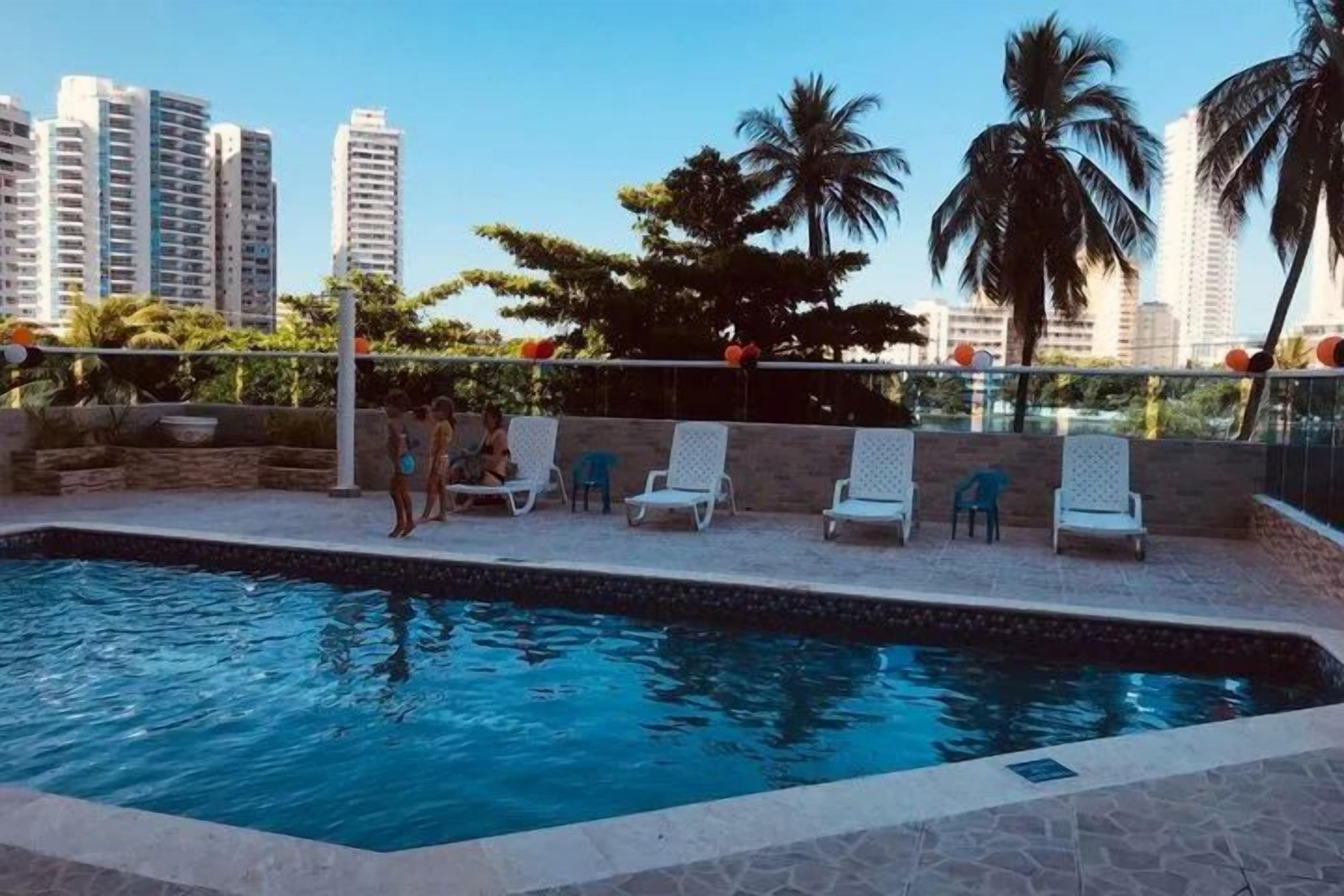 A swimming pool with lounge chairs and a cityscape in the background.