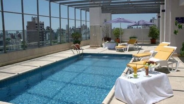 A rooftop pool with clear blue water, surrounded by lounge chairs and umbrellas, offering a city view. - Ariston Hotel (Rosario)