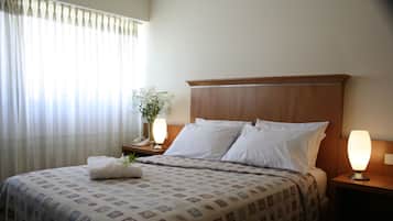 A neatly made bed with a patterned bedspread, a bedside lamp, and a vase with flowers on the nightstand.