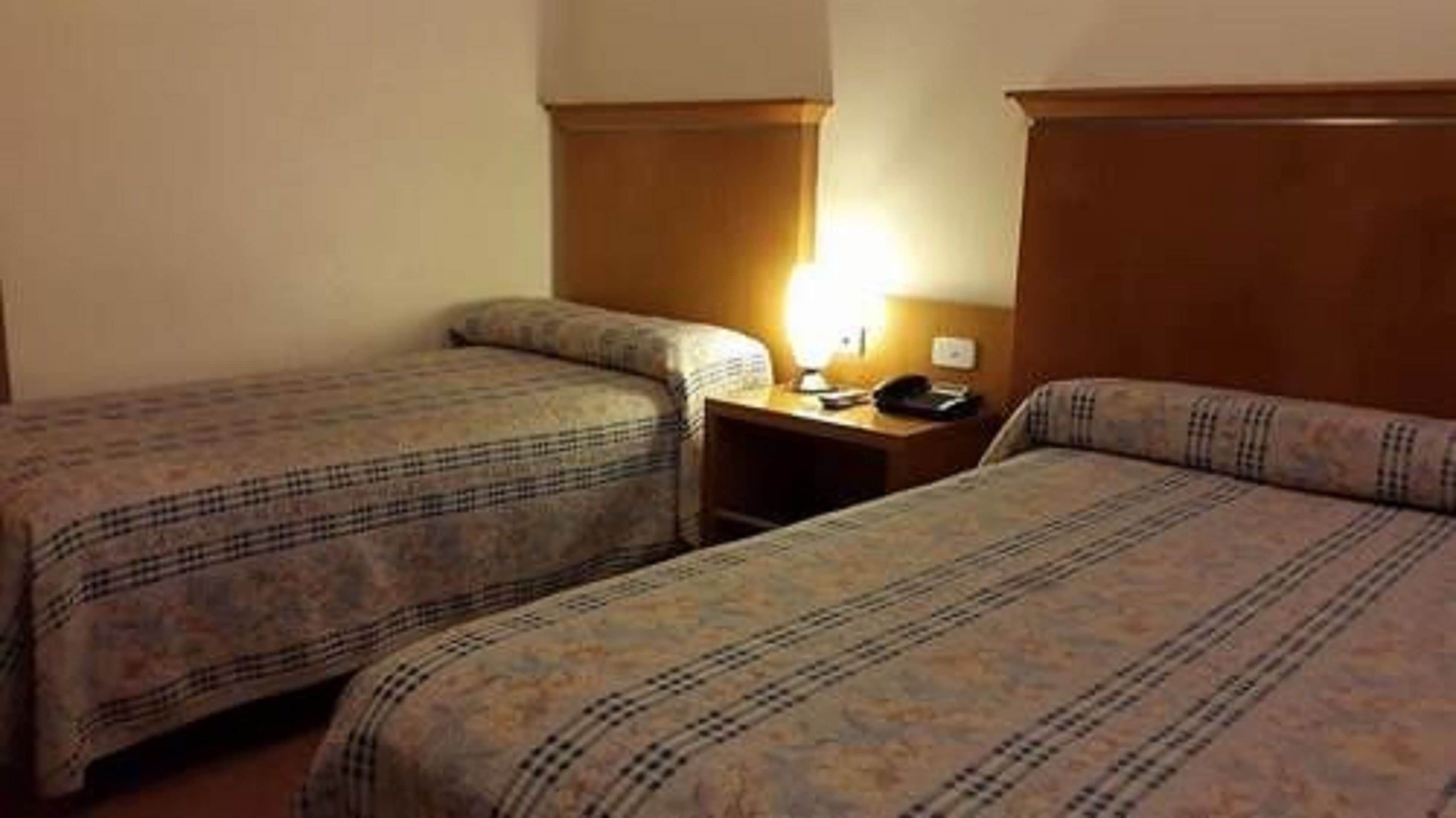 A hotel room with two single beds, a wooden headboard, a bedside table with a lamp, and a telephone.