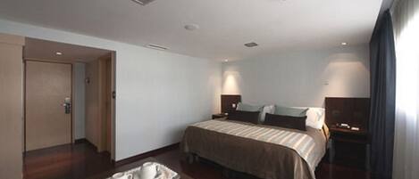 A hotel room with a bed, bedside tables, a tray with cups, and a door.