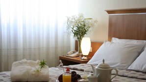 A neatly made bed with white linens, a tray with breakfast items, a vase with flowers, and a bedside lamp. - Ariston Hotel (Rosario)