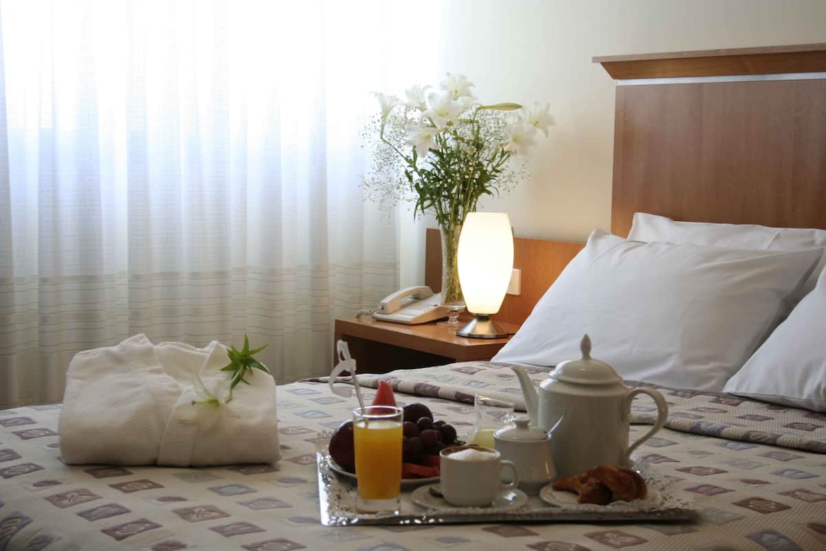 Ein ordentlich bezogenes Bett mit weißen Laken, ein Tablett mit Frühstücksangeboten, eine Vase mit Blumen und eine Nachttischlampe.