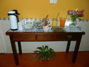 Uma mesa de madeira com diversos objetos, incluindo uma cafeteira, tigelas, um jarro e um vaso com flores.
