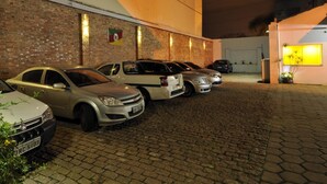 Ein Parkplatz mit mehreren in Reihe geparkten Autos, einer Backsteinmauer und einem Gebäude mit Tür und Fenstern.