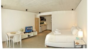 Ein kompaktes Hotelzimmer mit Bett, Schreibtisch inklusive Computer, einer kleinen Küchenzeile und einem Badezimmer.