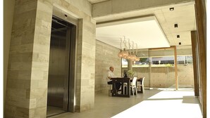Eine moderne Lobby mit Marmorwand, einem Aufzug, einer Glastrennwand und einem Tisch mit Stühlen.