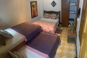 Un dormitorio con dos camas, un armario, un cuadro en la pared y una mesita con un jarrón.
