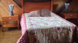 A bedroom with a wooden ceiling, a bed with a floral bedspread, two nightstands with vases, and a small drawer. - Bed & Breakfast Chaletico (San Jose)