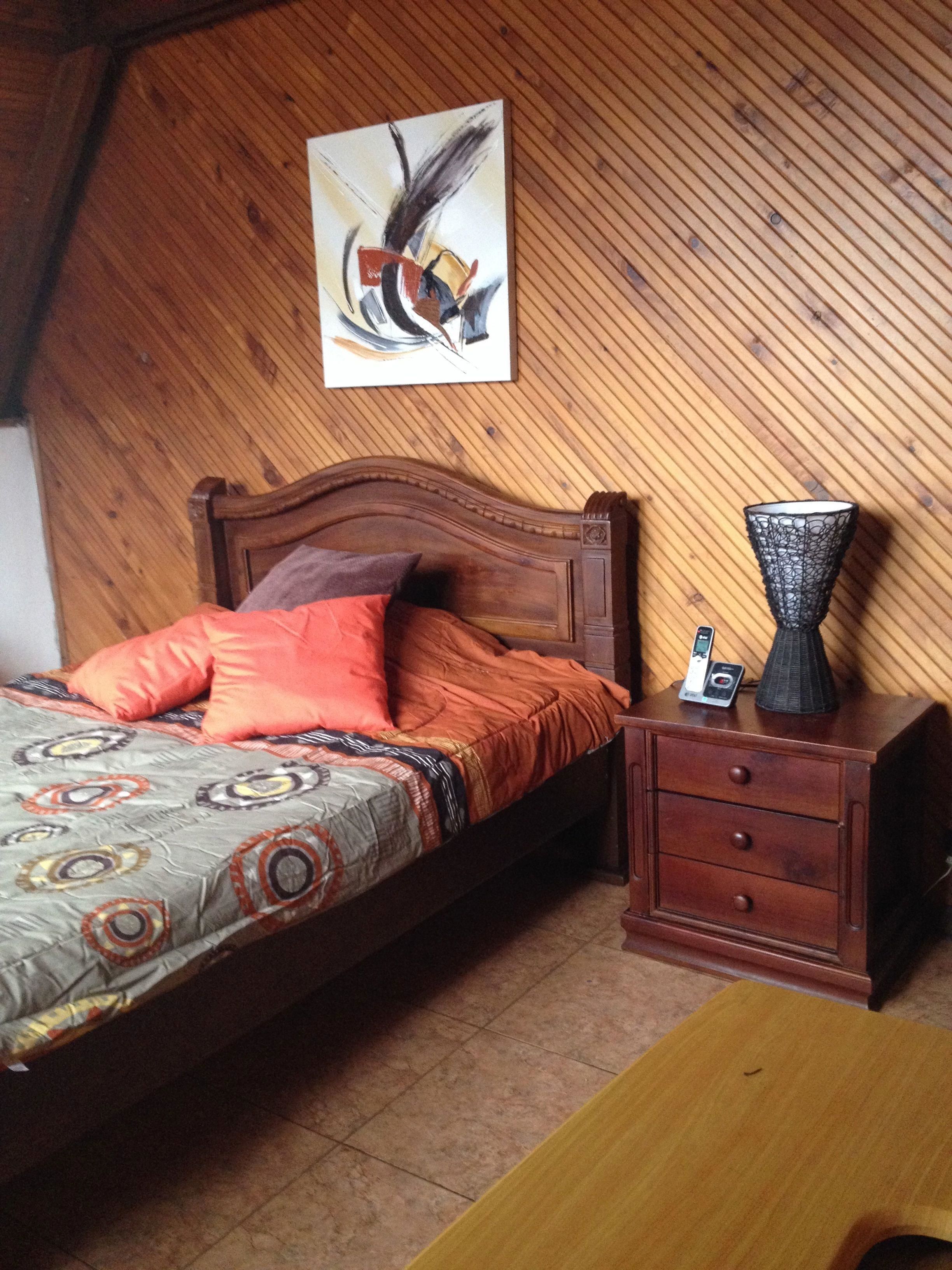Une chambre à coucher avec une tête de lit en bois, une couvre-lit à motifs, une table de chevet avec une lampe et un tableau accroché au mur.