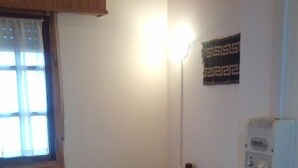 Ein kleines, schlichtes Zimmer mit einem Bett, einem Nachttisch, einer Lampe und einem Wandheizgerät.