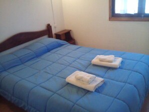 A bed with a blue quilt and two folded towels. - Hotel Residencial Eurostop (Villa General Belgrano)