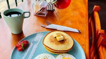Un plato de desayuno con huevos, tocino, panqueques y una fresa.