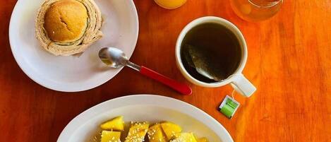 Une table mise pour le petit-déjeuner avec une assiette de crêpes, un verre de jus d’orange, une tasse de thé et un bol de morceaux de mangue.