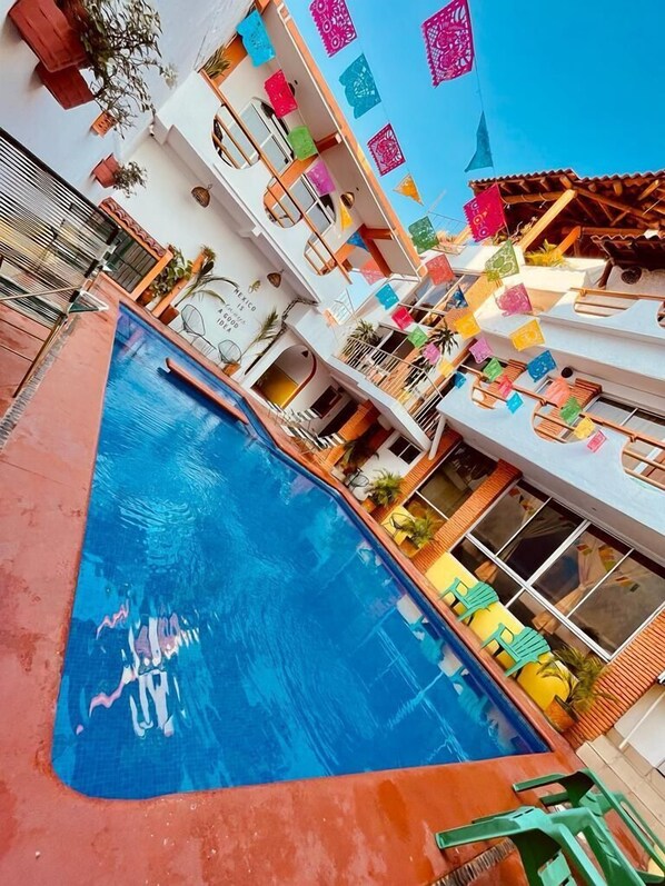 A multi-level hotel with a central swimming pool, balconies with colorful decorations, and a clear blue sky. - Hotel Casa de la Palma Bed and Breakfast (Zihuatanejo)