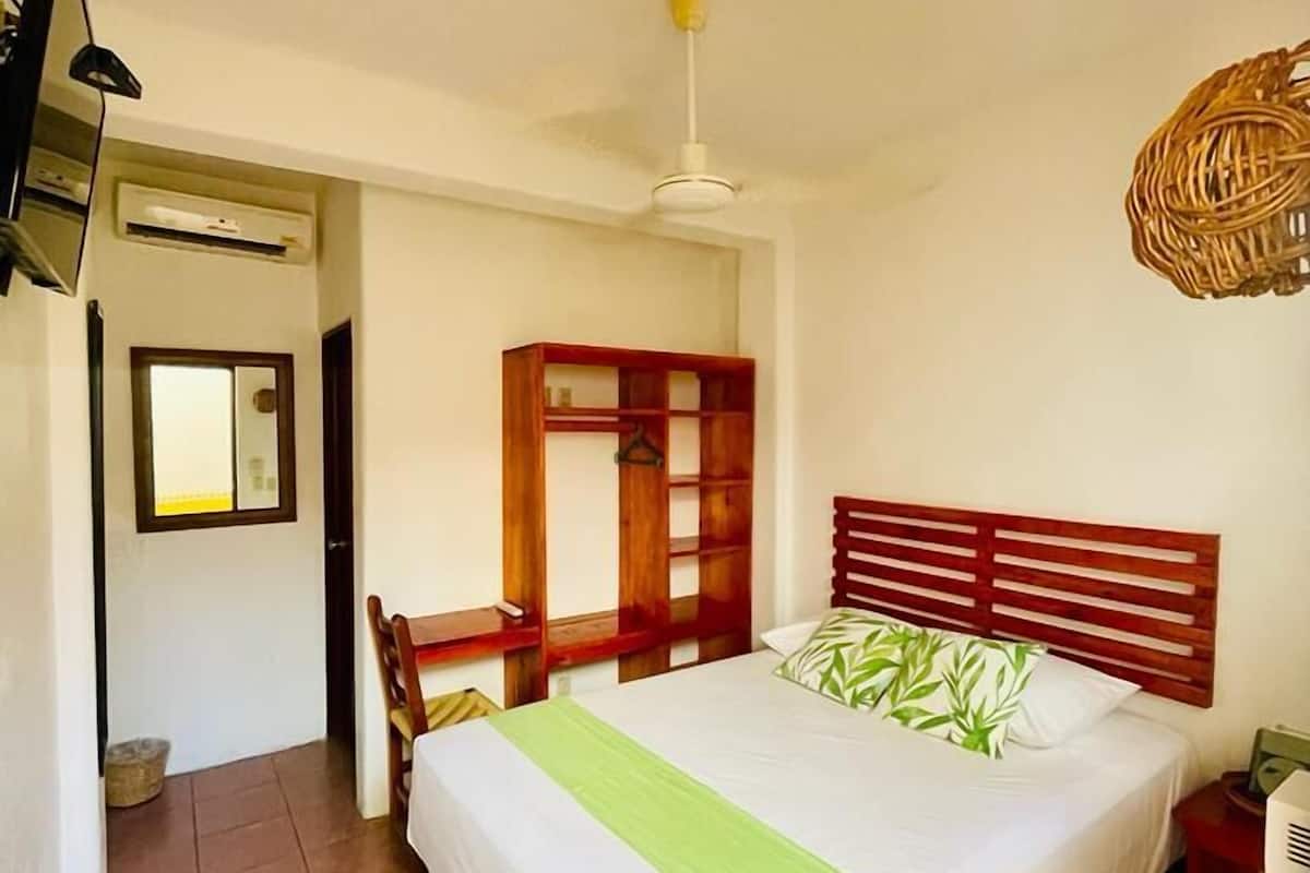 Un dormitorio con cama, un armario de madera, una silla, un televisor y un ventilador de techo.