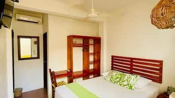 A bedroom with a bed, a wooden wardrobe, a chair, a television, and a ceiling fan.