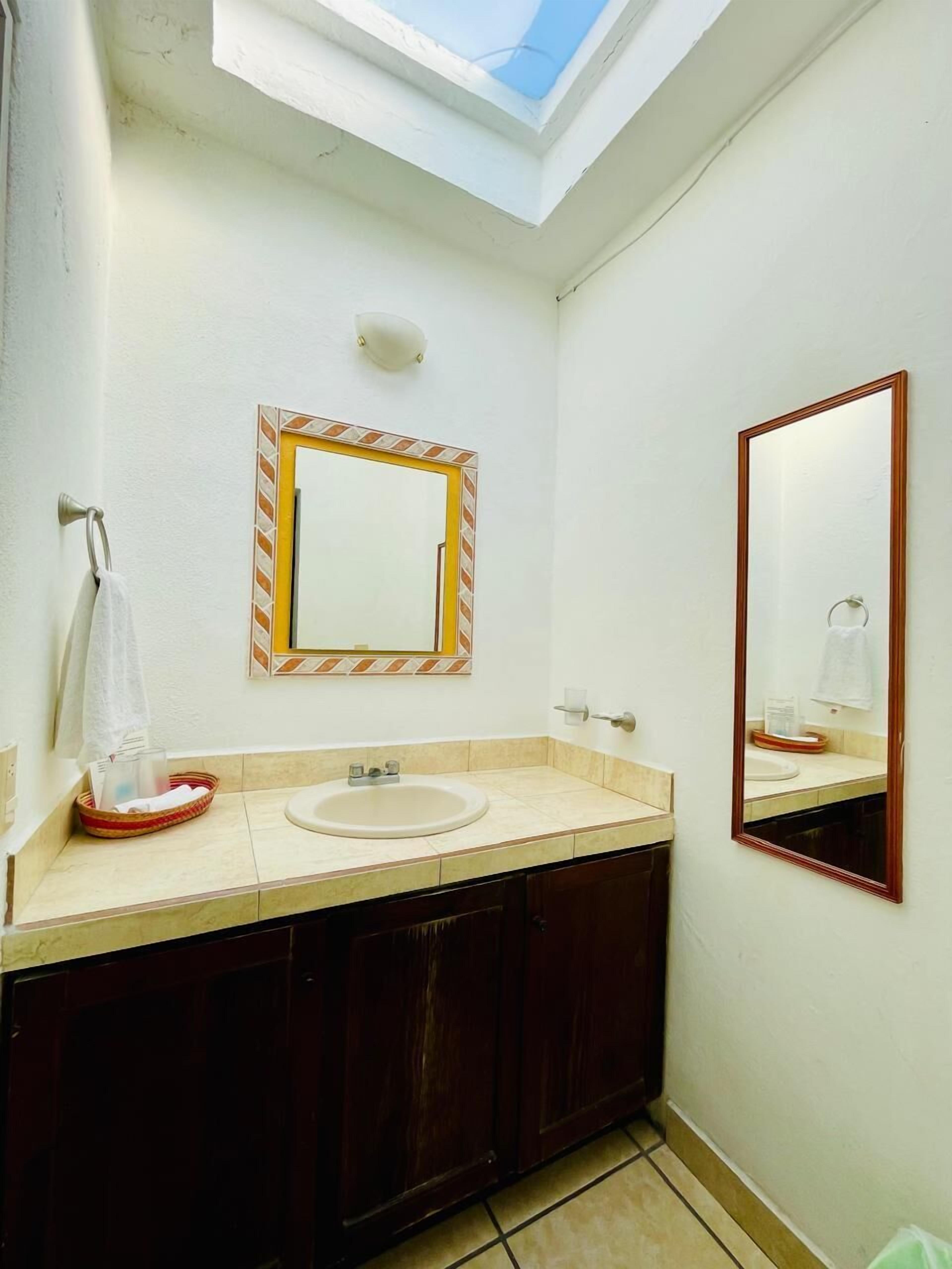Un baño con tragaluz, un lavamanos, un espejo y un perchero para toallas.