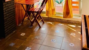 A cozy patio area with a wooden table and chairs, a television mounted on the wall, and a view of the outside through yellow curtains. - Hotel Casa de la Palma Bed and Breakfast (Zihuatanejo)