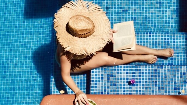 A person sitting by a pool with a straw hat and a book, holding a plate with watermelon slices. - Hotel Casa de la Palma Bed and Breakfast (Zihuatanejo)