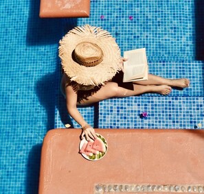 A person sitting by a pool with a straw hat and a book, holding a plate with watermelon slices. - Hotel Casa de la Palma Bed and Breakfast (Zihuatanejo)