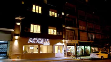 Um hotel chamado "ACQUA HOTEL" com letreiros iluminados, entrada visível e uma bicicleta estacionada na frente.