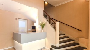 A reception area with a modern desk, a staircase, and a potted plant. - Acqua Hotel (Mar del Plata)