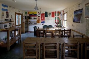 Een kamer met een houten eettafel en stoelen, een keukenhoek met een magnetron, en verschillende vlaggen aan de muren.