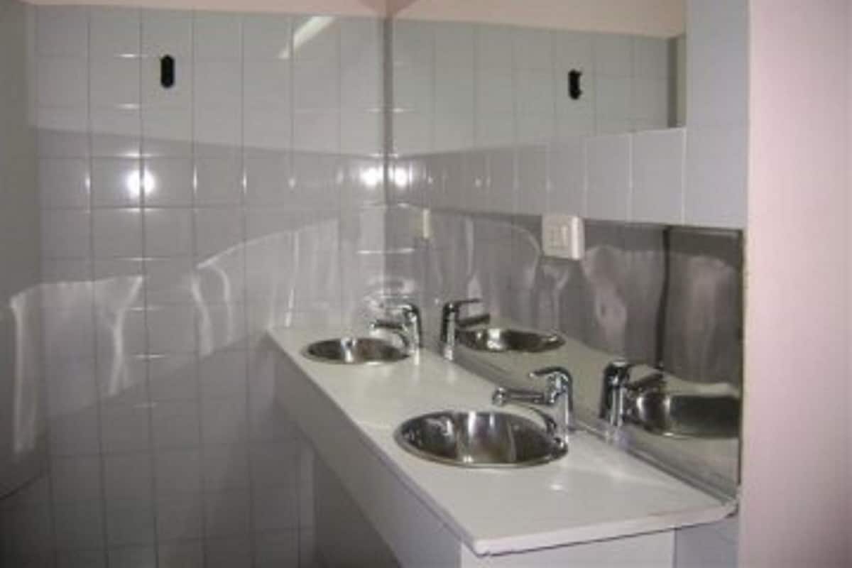 Un baño con paredes de azulejos blancos, encimera blanca y dos lavamanos con grifos.