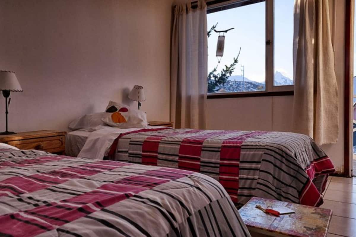 Habitación de hotel con dos camas, una mesita de noche, una lámpara, una pequeña mesa y una ventana con cortinas.