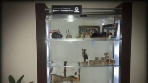 A glass display case with various items including jars, a toy car, and figurines.