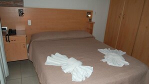 A neatly made bed with a brown bedspread, a bedside table with a lamp, and a wooden wardrobe.