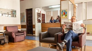 Un hombre sentado en un sofá de cuero leyendo una revista en un vestíbulo moderno con piso de madera y un mapa en la pared.