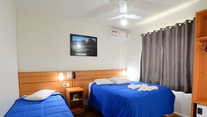 Habitación de hotel con dos camas, cabeceros de madera, ventilador de techo, un cuadro enmarcado en la pared y una ventana con cortinas.