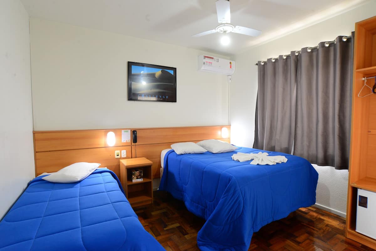 A hotel room with two beds, wooden headboards, a ceiling fan, a framed picture on the wall, and a window with curtains.