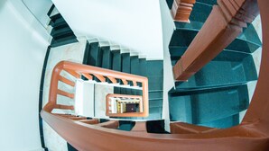 A spiral staircase with a wooden handrail and a white wall. - Angkor Udom Guesthouse (Siem Reap)