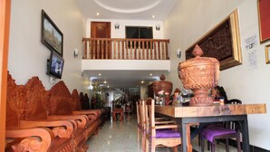 A spacious hotel lobby with a high ceiling, a wooden staircase, and a large ornate table with chairs. - Angkor Udom Guesthouse (Siem Reap)