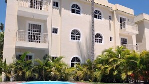 Un hôtel à plusieurs étages doté d’une piscine, de palmiers et surplombant un ciel d’un bleu limpide.
