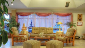 A living room with a sofa set, two armchairs, a coffee table, and a view of a temple through large windows. - Hotel Salerno (Villa Carlos Paz)