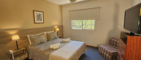 A hotel room with a bed, bedside lamps, a ceiling fan, a window with a view, a television, and a small seating area.