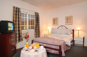 A hotel room with a bed, bedside lamps, a TV on a wooden cabinet, a table with breakfast items, and two framed pictures on the wall. - Hotel Salerno (Villa Carlos Paz)