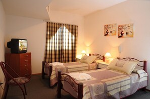 A hotel room with two beds, a TV, a chair, and a window with curtains. - Hotel Salerno (Villa Carlos Paz)